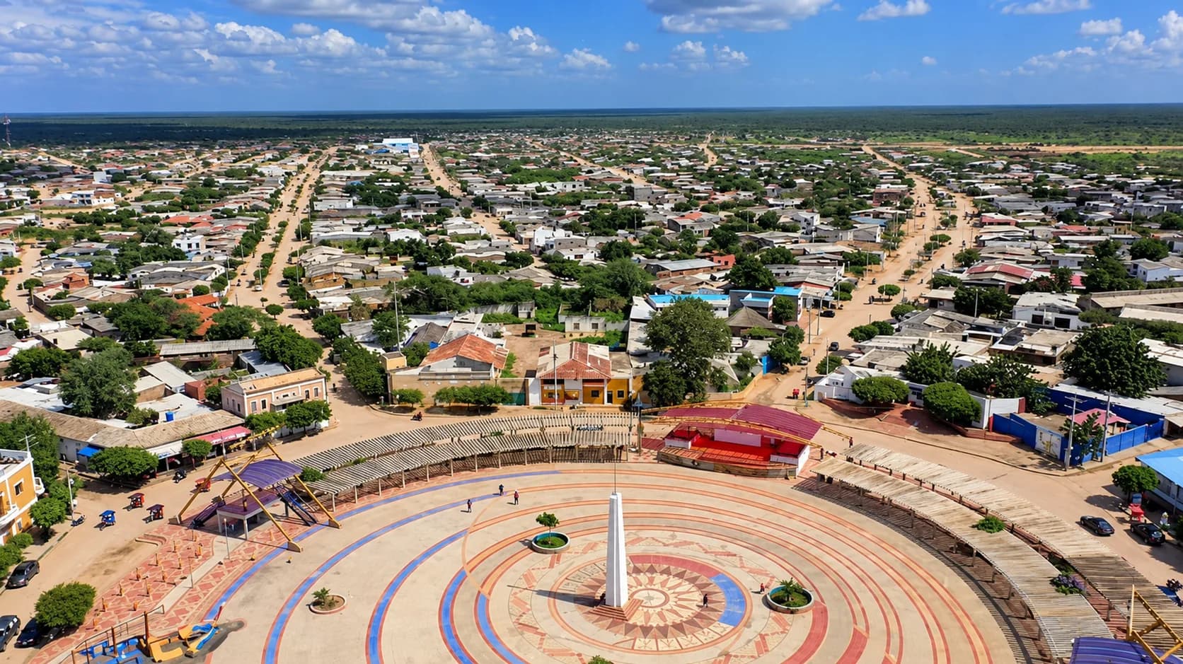 Ilustración aérea de una plaza circular con obelisco en un pueblo de casas bajas en paisaje semiárido