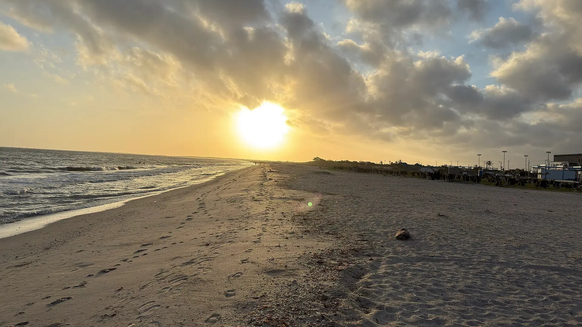 Amanecer en la playa de Riohacha, con huellas en la arena y el sol sobre el mar